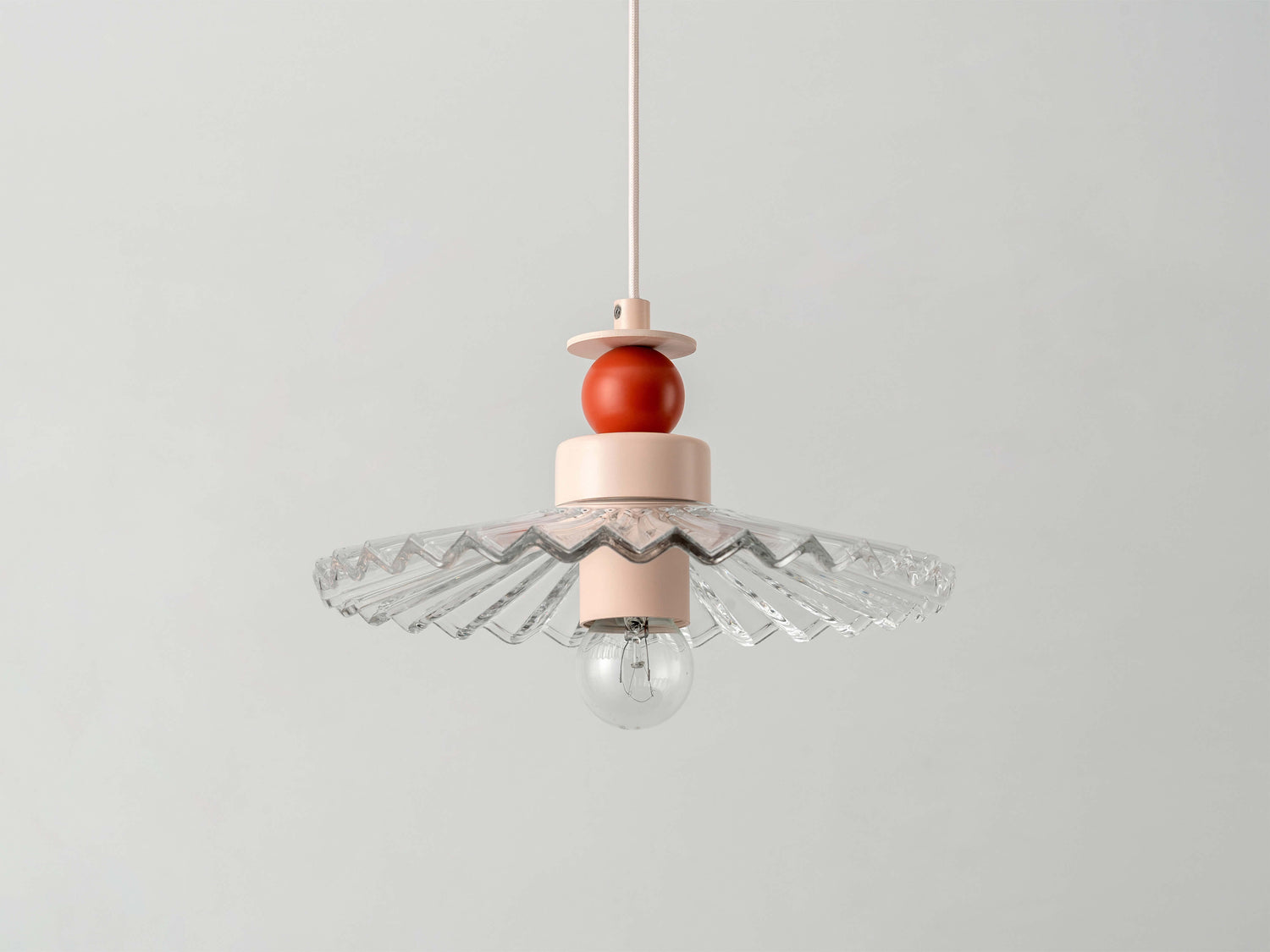 A fluted, ribbed glass shade is stacked with burnt orange and pale pink painted metal disk and ball elements, hanging from a ceiling pendant.
