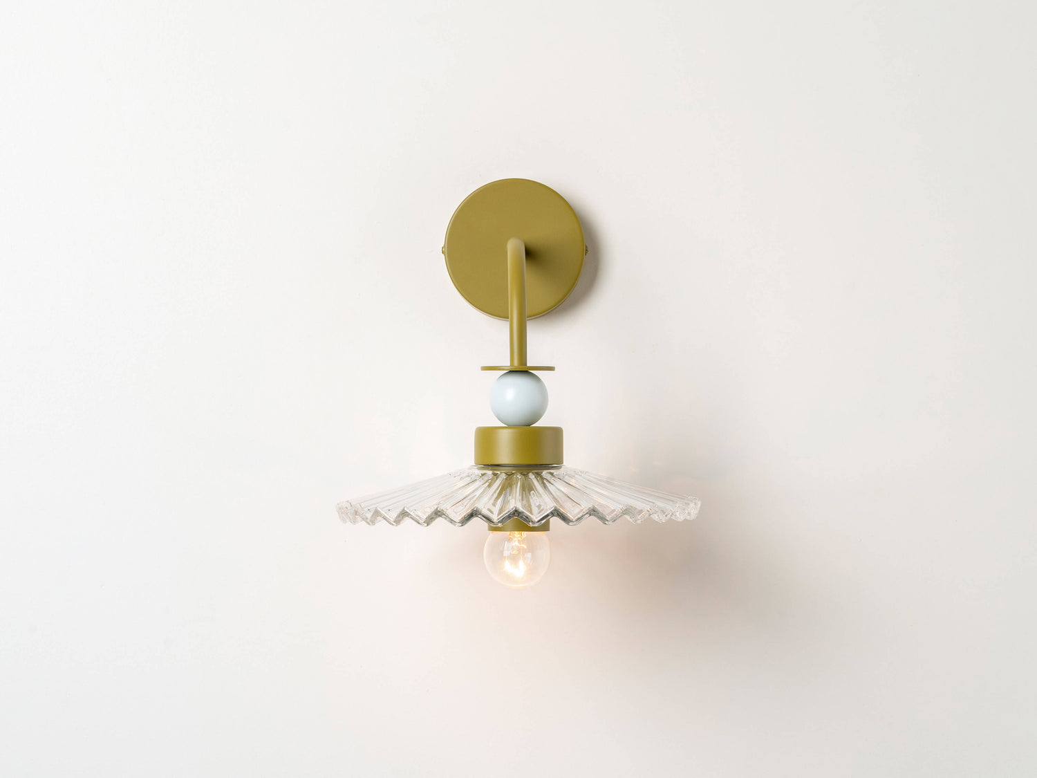 A fluted, ribbed glass shade is stacked with moss green and pale blue painted metal disk and ball elements, hanging from a wall fixture. Light is on.