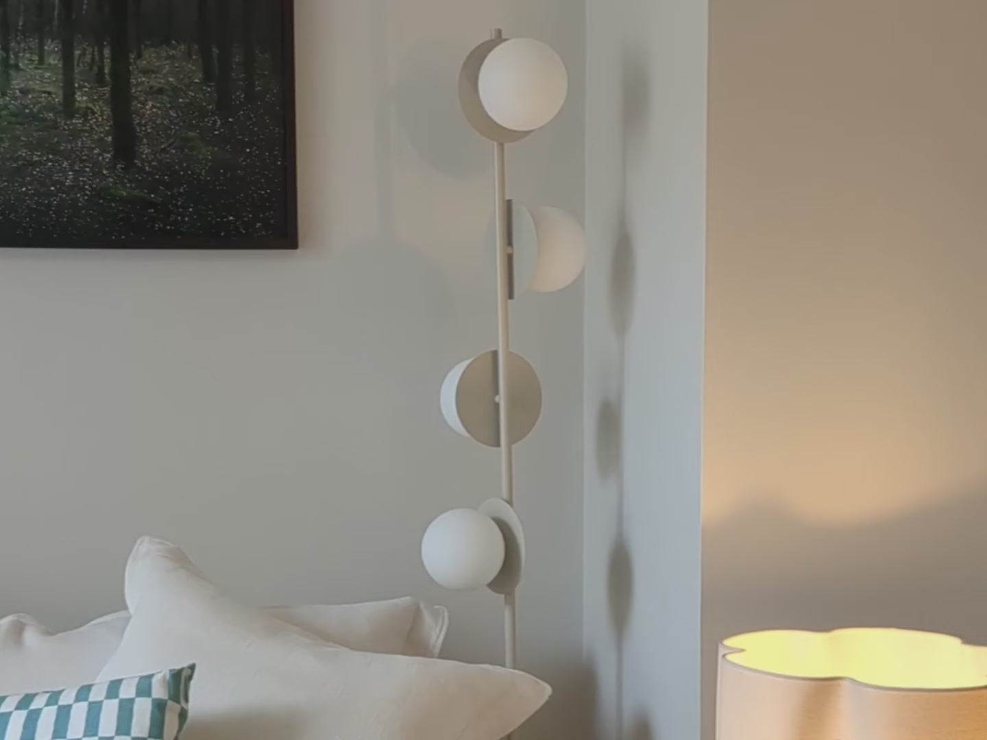 A vertical sand-coloured metal stem holds 4 metal disks at varying angles, each topped with an opal glass shade. Light is positioned in a living room beside a sofa..