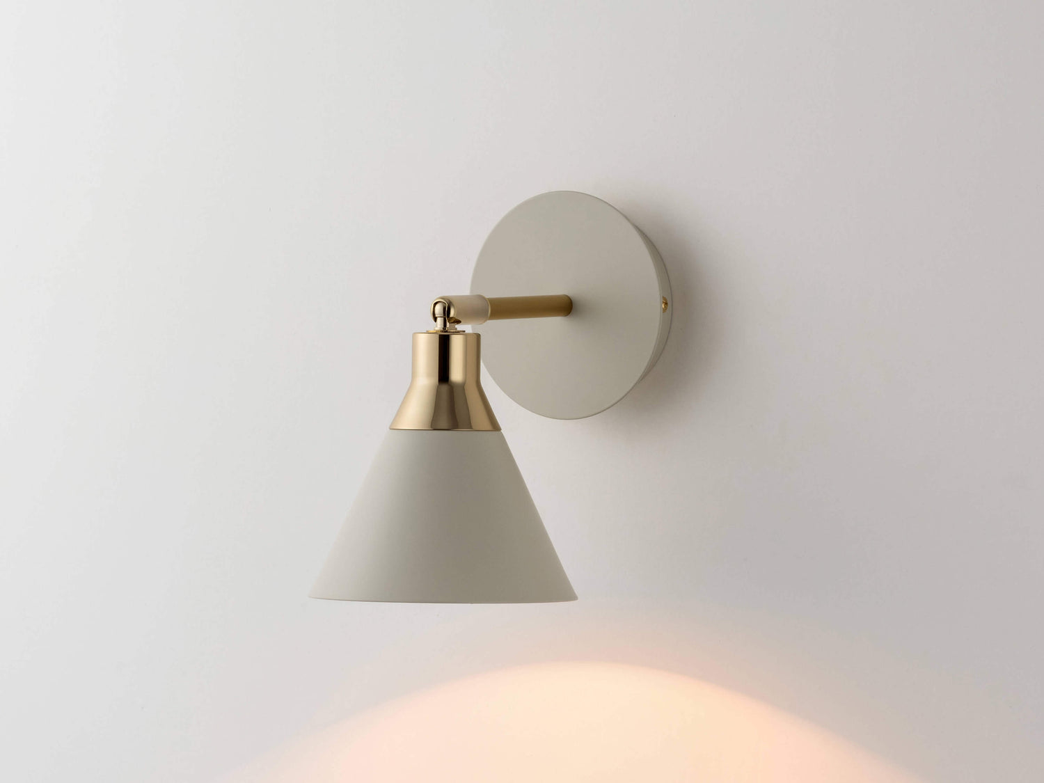 An adjustable sand metal cone shade is attached to a sand wall fixture with brass cap details. Light is on.