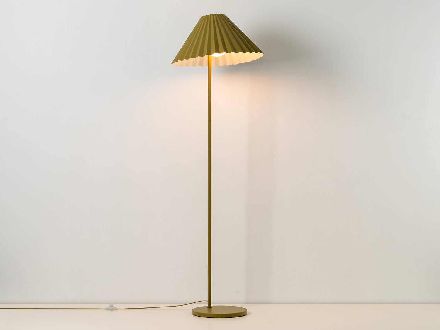 A floor lamp with a fluted, pleated metal shade that can be tilted and adjusted. It is painted moss green, with a contrasting pale blue colour inside the shade. The light is on.
