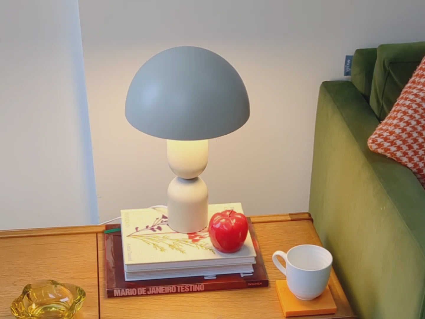 Sand mushroom dome table lamp on a coffee table beside a green velvet sofa. 