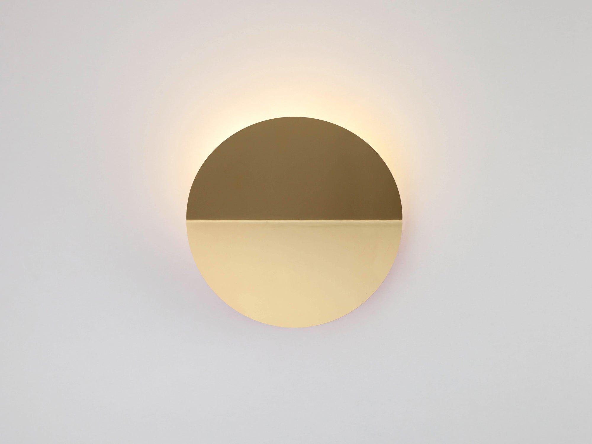A brass circular wall light that sits flush to the wall, with a subtle fold and integrated LED bulbs.