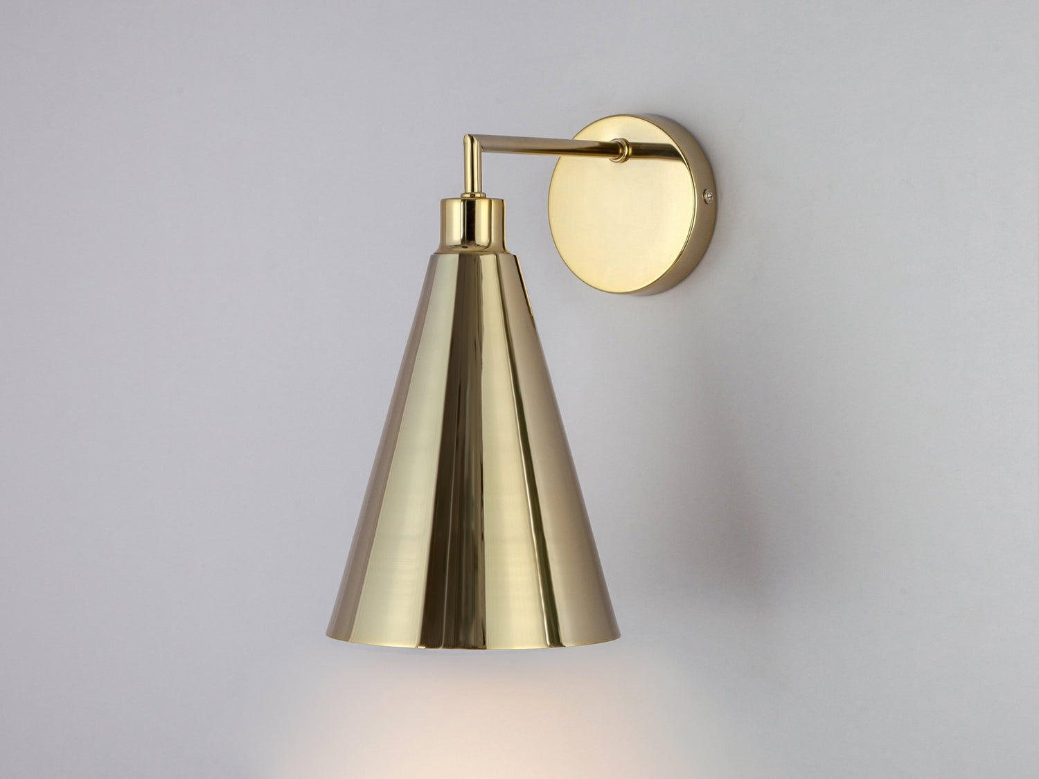 A brass wall fixture suspends a cone-shaped brass metal shade.